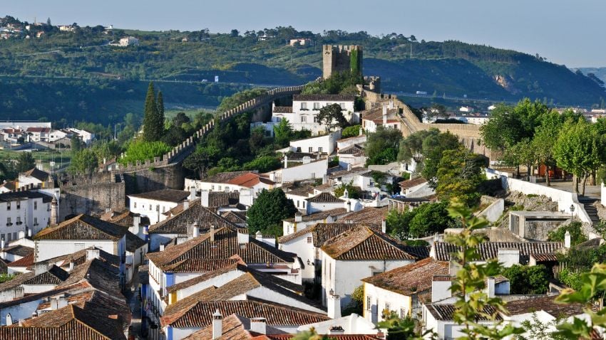 Whitewashed houses and colourful trim highlight one of the best places to visit in Portugal for picturesque villages /Óbidos is a medieval walled town, which is small enough to walk from one end to the other in about fifteen minutes. The fascinating thing is that the walls are still intact