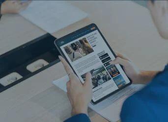 Person reading financial and offshore news articles on a tablet at a desk, representing access to global insights and consulting expertise.