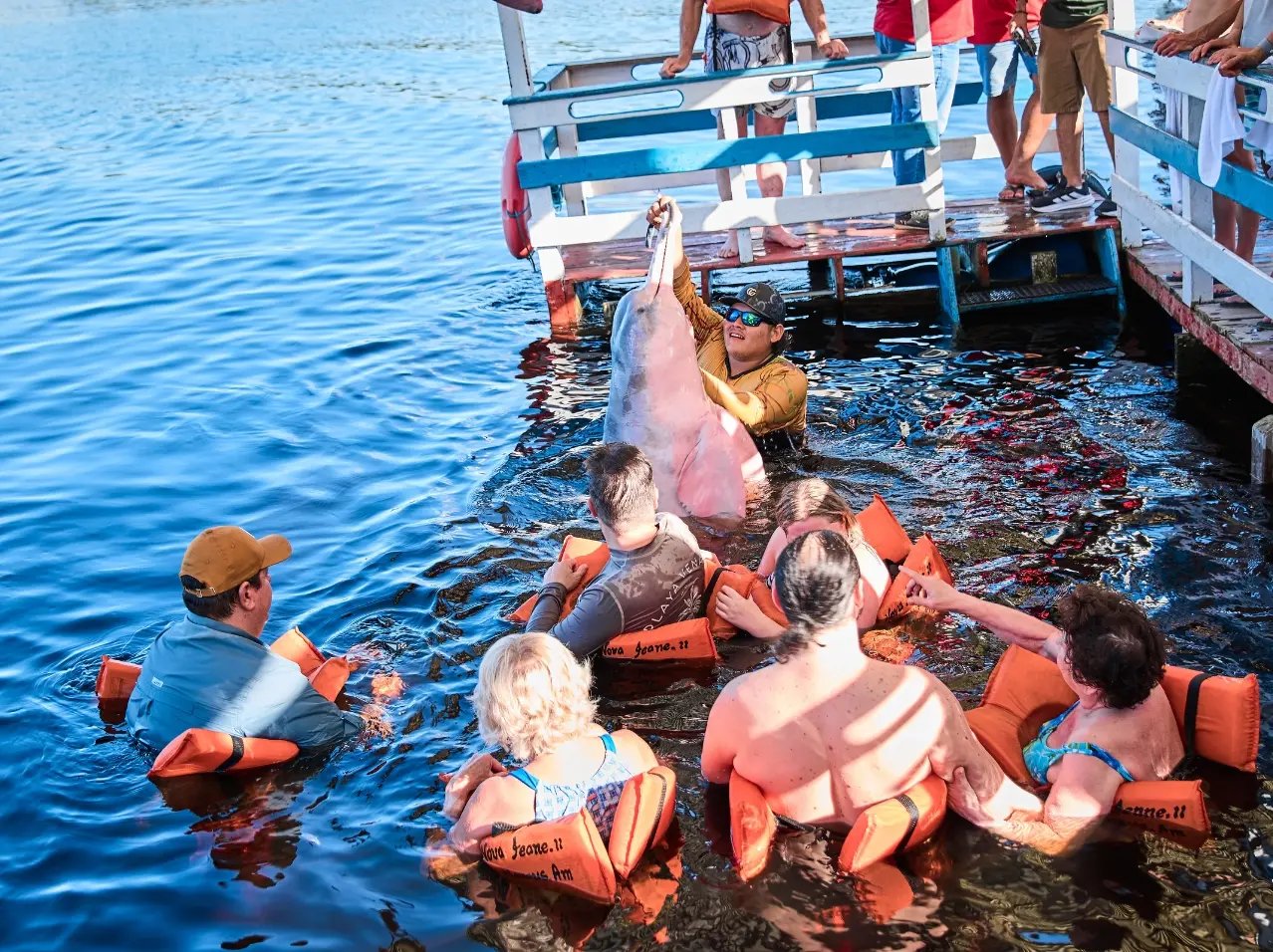 A group of clients and friends in a river with a guide holding a pink river dolphin