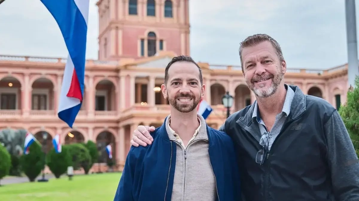 Mikkel Thorup and Patrick Hiebert posing together outdoors in front of a grand pink historic building with Paraguayan flags in the background.