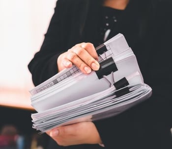 A person holding a large stack of papers organized with black binder clips.