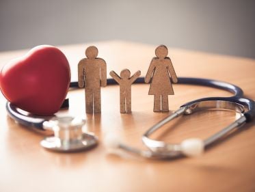 Symbolic representation of family health insurance with wooden figures of a family, a red heart, and a stethoscope on a table.